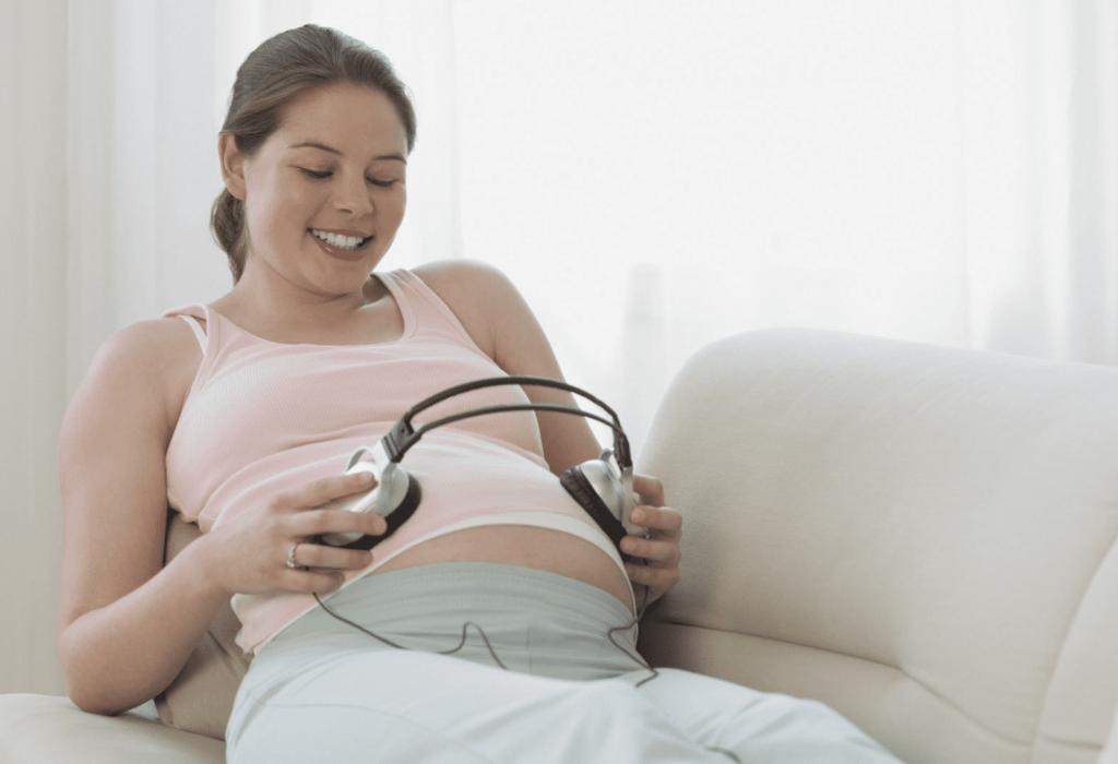 Una embarazada coloca unos cascos sobre su barriga